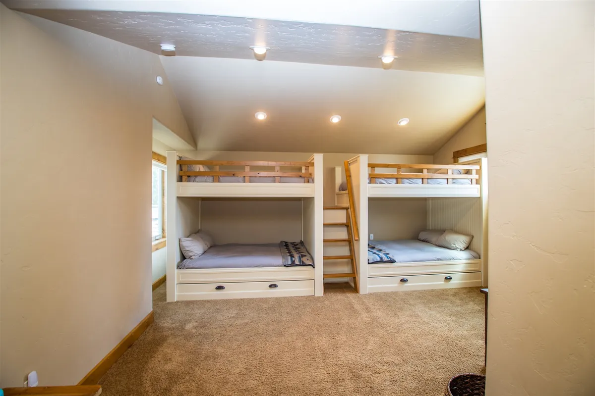 This image showcases a cozy bunk room featuring sturdy bunk beds, a soft carpeted floor, and inviting windows that let in plenty of natural light. The family-friendly setup is ideal for children, highlighting the playful and functional sleeping arrangements.
