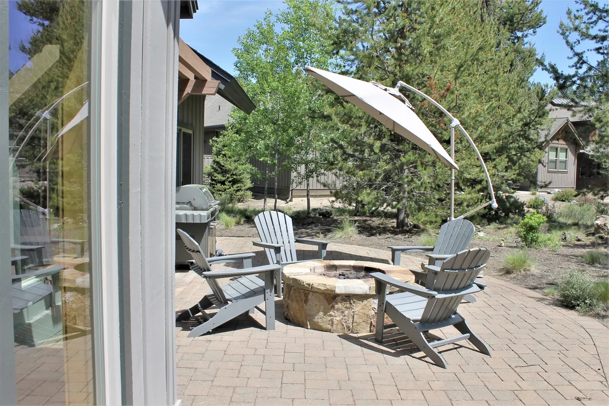 An inviting outdoor fire pit surrounded by Adirondack chairs and a large umbrella, set amid lush landscaping. The space is designed for evening gatherings, storytelling, and enjoying beautiful sunsets with family and friends.