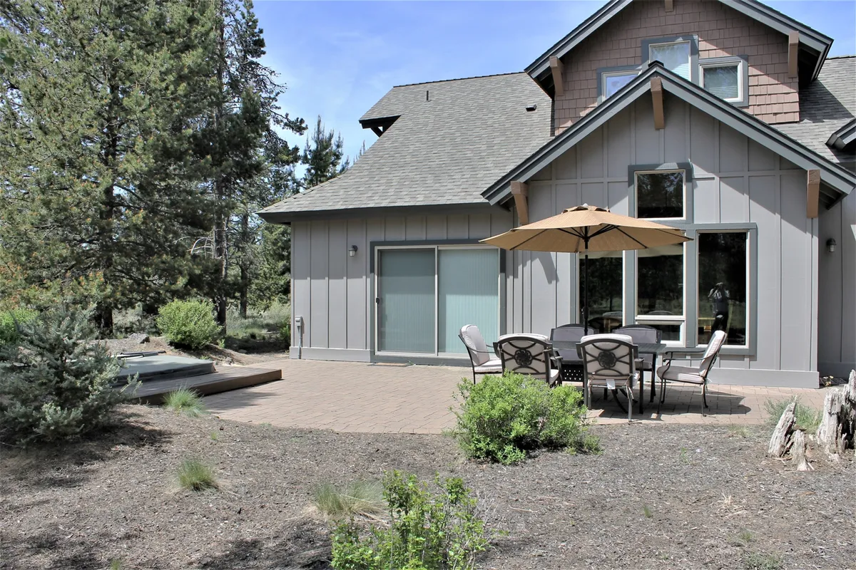 A peaceful patio with a table and chairs shaded by an umbrella, surrounded by greenery. The area invites outdoor dining, morning coffee, or a quiet moment after a day of exploring the community.
