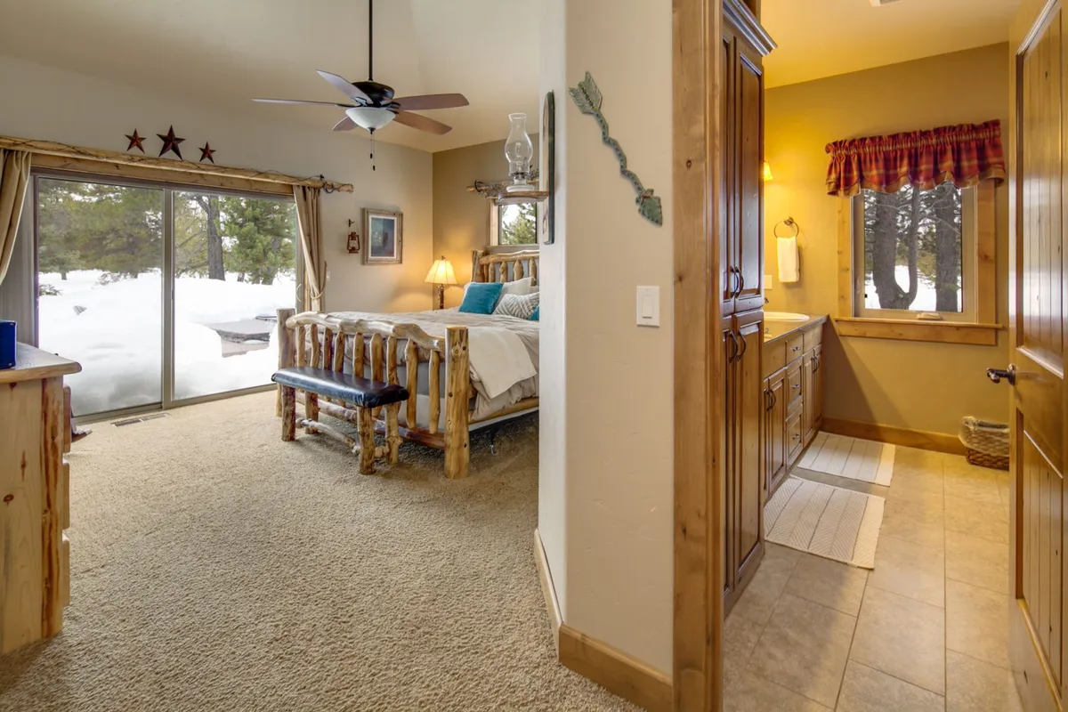 A bedroom featuring a cozy log cabin bed, large windows with wooden trim, cabinetry, and soft decorative accents. The room feels peaceful and serene, with natural light streaming in, highlighting the comfortable and thoughtfully designed space.