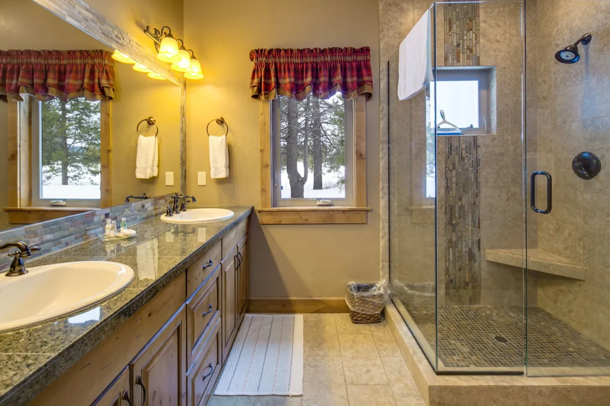 A bright bathroom with a double vanity, glass shower enclosure, and large windows letting in ample daylight. Modern fixtures and natural finishes create a calming, spa-like environment, perfect for morning routines or unwinding after an active day.