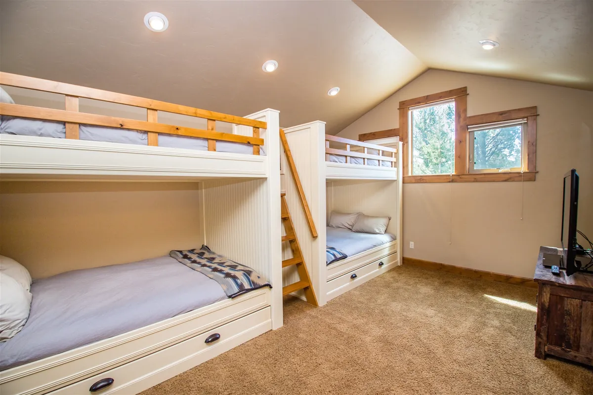 This inviting space features multiple bunk beds with plush bedding, large windows streaming in sunlight, and a wall-mounted television. The warm, cozy environment fosters memorable sleepovers and relaxed downtime for kids.