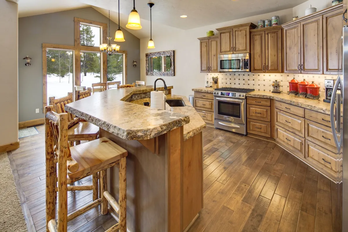 A modern kitchen is featured, boasting a spacious island, warm wooden cabinetry, sleek stainless steel appliances, and large windows that fill the space with natural light. The design merges functionality with style, perfect for preparing gourmet meals or gathering with family and friends.