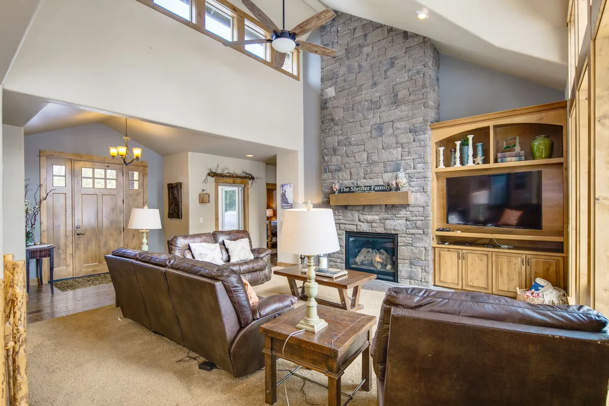 The hero image showcases a spacious living area with a stunning stone fireplace as the centerpiece, framed by expansive windows that fill the room with natural light. Plush, comfortable seating invites guests to relax, while warm wood accents create a cozy, inviting ambiance ideal for family gatherings or unwinding after outdoor adventures.