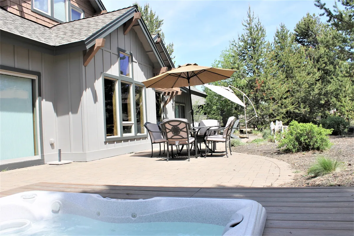 A welcoming patio scene featuring a jacuzzi, an outdoor dining set with an umbrella, and views of the surrounding landscape. The mood is tranquil and inviting, ideal for morning coffee or relaxing at sunset.