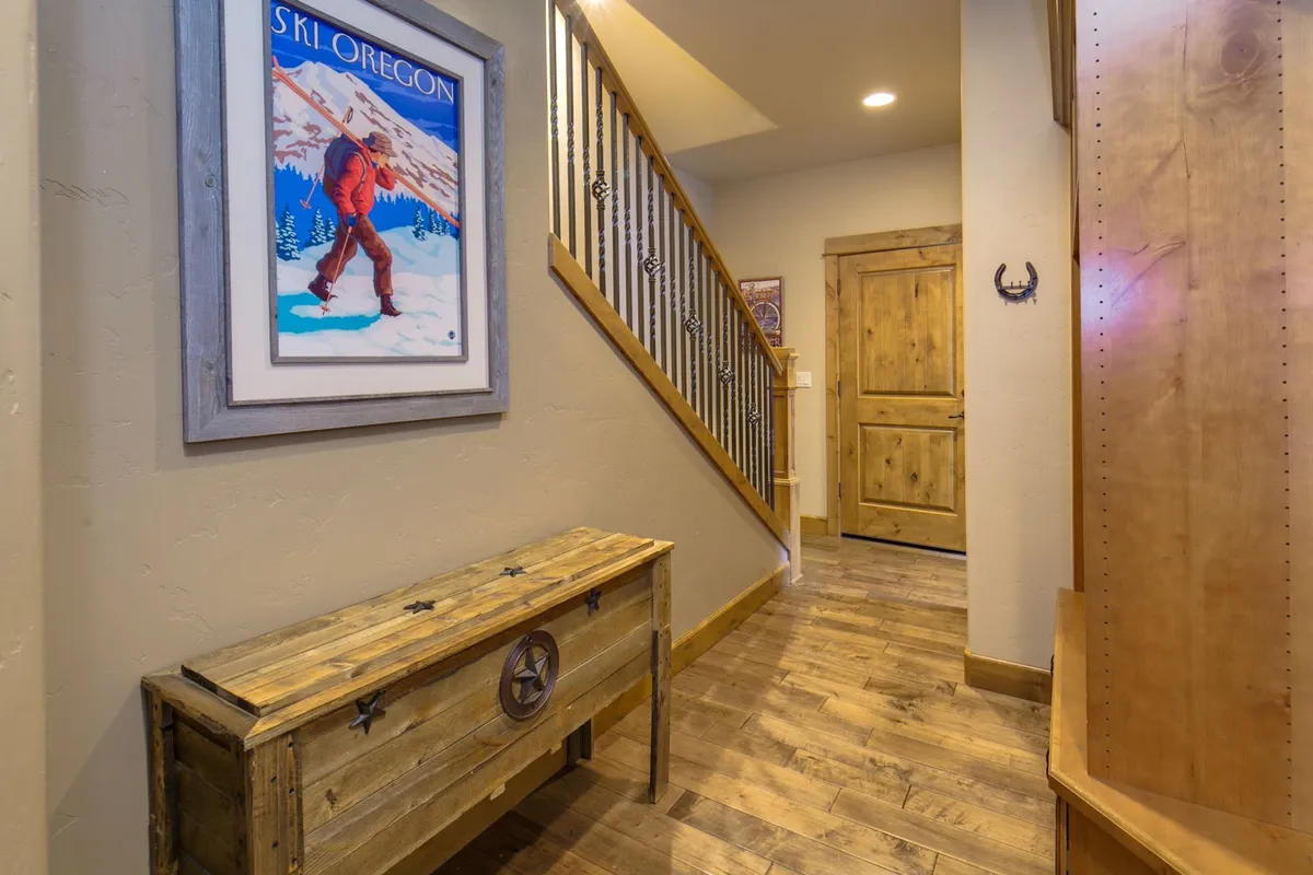 A welcoming entryway features a rustic wooden bench, a prominent ski poster on the wall, and a staircase leading to the living areas. The space evokes the feeling of returning from a day spent outdoors, with practical storage and a nod to adventure sports in the decor.